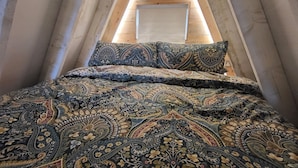 Un dormitorio acogedor en el ático con techo inclinado, estructura de cama de madera y colcha estampada.