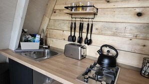 Una cocina con pared de madera, un lavamanos, un tostador, una tetera y utensilios colgantes.
