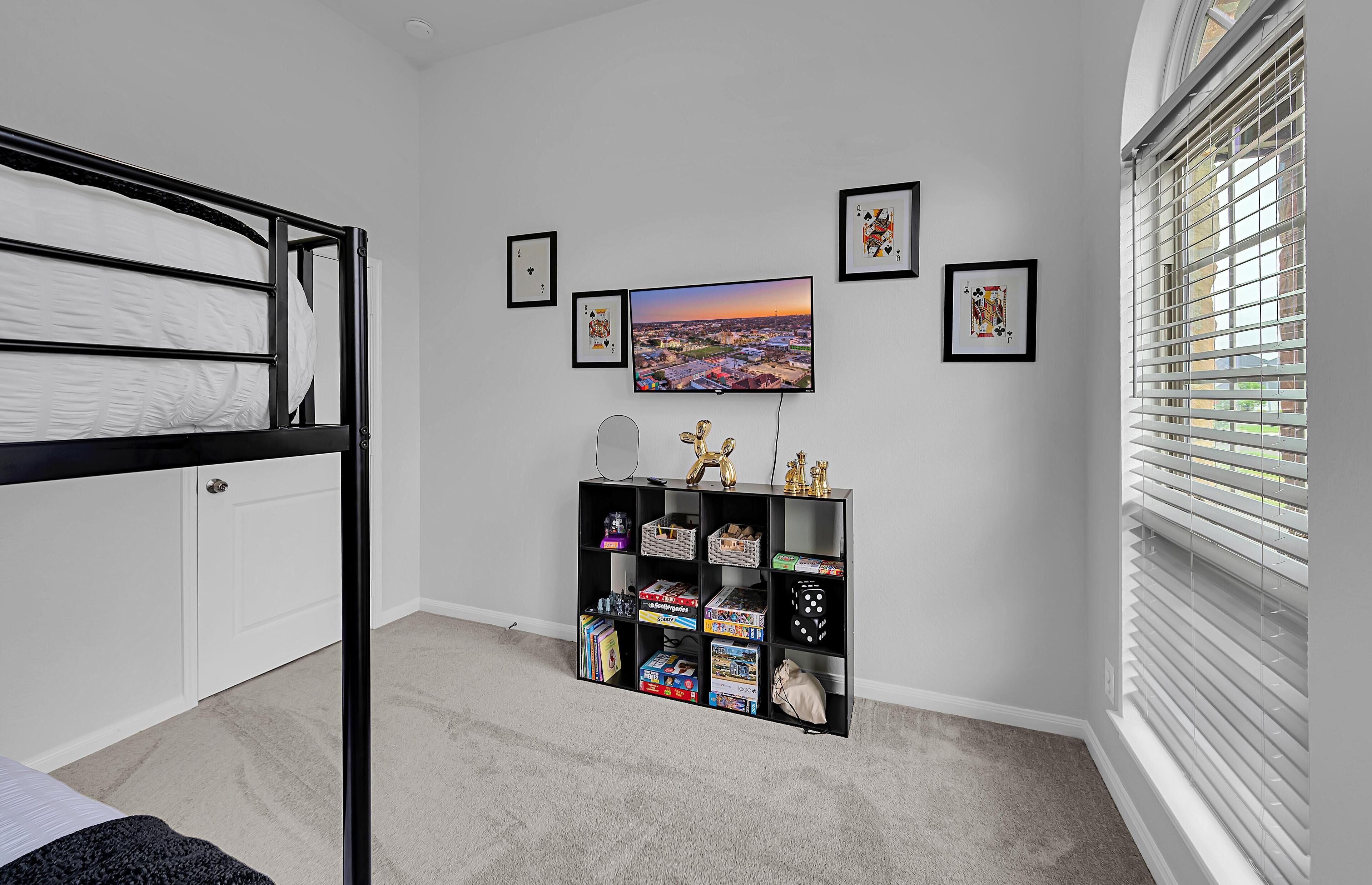 A bedroom with a bunk bed, a TV mounted on the wall, and a shelf with board games.