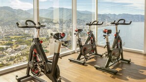 Tres bicicletas estáticas en una sala con ventanas amplias que dan a una ciudad y montañas.