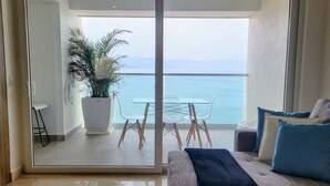 Un balcón con una mesa y sillas de vidrio, una planta en maceta y vista al mar.