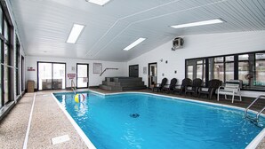 En indendørs swimmingpool med klart vand, et skilt med røgfri zone og en trappe, der fører til en etage over.