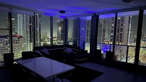 A modern living room with a dining area, large windows offering a city view, and a blue ambient light. - Miami downtown Amazing view rooftop pool & jacuzzi (Miami)