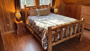 A wooden bedroom with a bed, two bedside lamps, a dresser, and a window with curtains.
