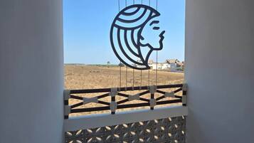 Un balcone con un recinto a motivi geometrici, un tetto di paglia e il profilo di una donna in controluce.