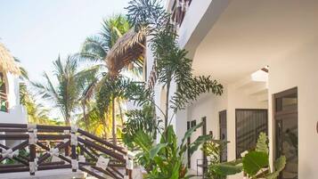 Zona de piscina con vista despejada al agua, rodeada por un edificio blanco con balcón y palmeras.