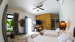 A hotel room with two beds, a ceiling fan, a television, a potted plant, and a large window.