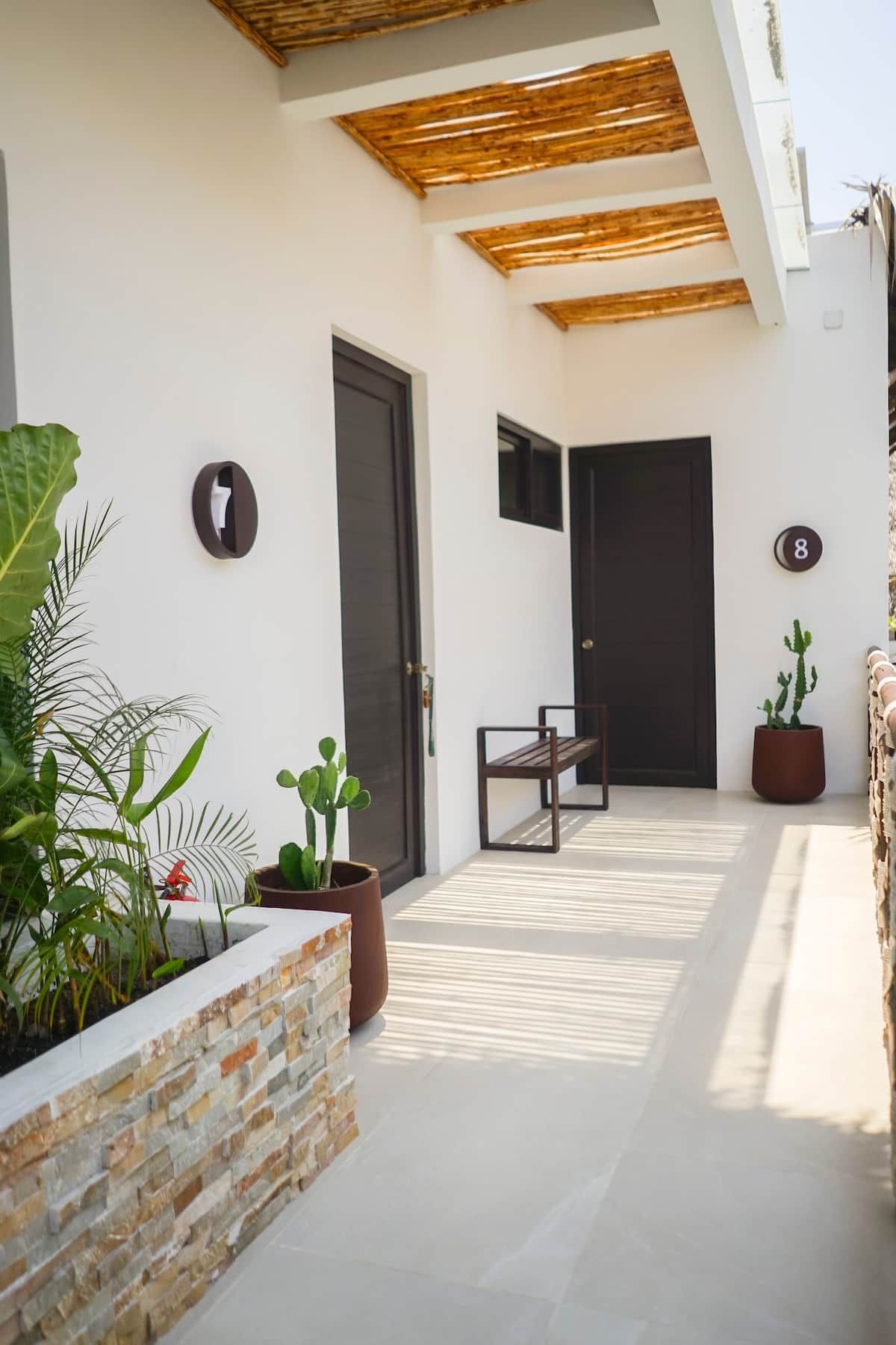 A modern outdoor area with a bench, potted plants, and a door with a number.