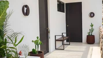 A modern outdoor area with a bench, potted plants, and a door with a number.