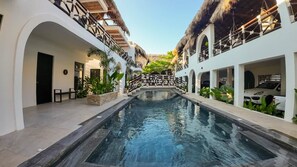 Un área de piscina con un elemento acuático central, rodeada de paredes blancas y estructuras con techo de paja.