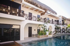 A resort with a swimming pool, multiple balconies, and a thatched roof.