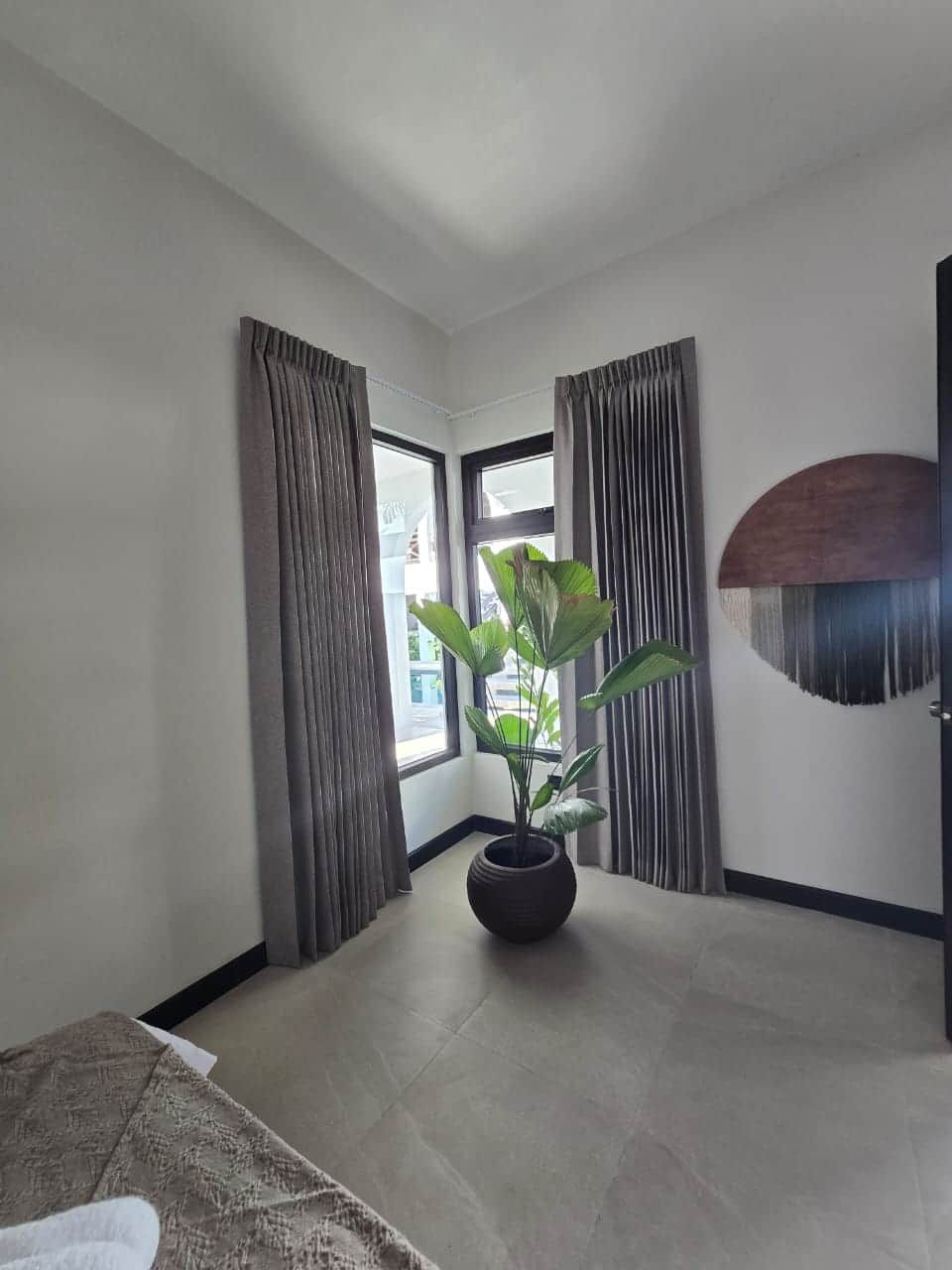 A room with a large window, a potted plant, and a wall-mounted decorative piece.