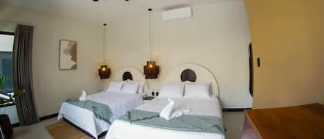 Habitación de hotel con dos camas, ventilador de techo, luces fijadas a la pared y una mesita de noche de madera.