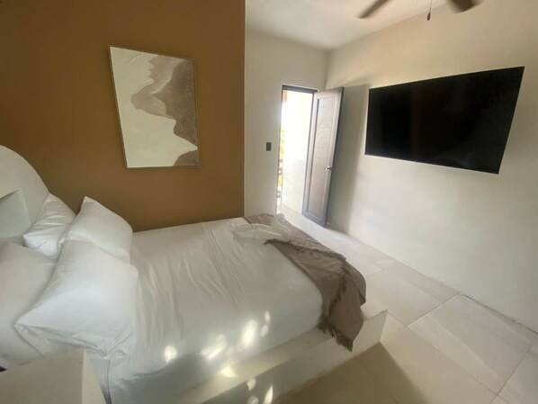 A bedroom with a bed, a flat-screen TV mounted on the wall, and a door leading to a balcony.
