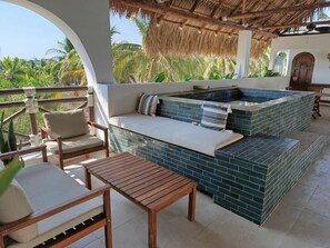 A rooftop terrace with a hot tub, seating area, and a view of palm trees.