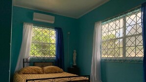 A room with a bed, a statue, and two windows with curtains. - Jude Apartments - 3-bedroom apartment with AC in  Soufrière (Soufrière)