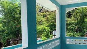 A covered outdoor area with teal walls and white decorative panels, featuring large windows overlooking a lush garden. - Jude Apartments - 3-bedroom apartment with AC in  Soufrière (Soufrière)