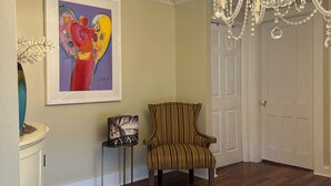 A room with a wooden floor, a striped armchair, a chandelier, and a framed abstract painting on the wall.