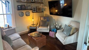 A living room with a sofa, armchairs, a coffee table, a TV, framed pictures on the wall, and a lamp.