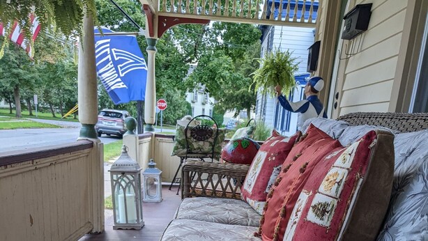 A wicker sofa with patterned cushions on a porch, a wicker table with a glass of red drink, and a stop sign in the background.