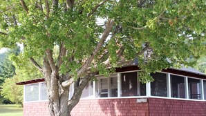 Een rode houten woning met een grote boom ervoor, een overdekte veranda en een bordje met de tekst 'Beechnut'.