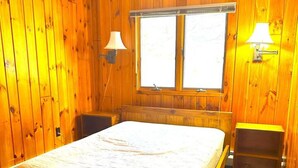 Una habitación con paneles de madera, una cama individual, dos mesitas de noche y una ventana con vistas.