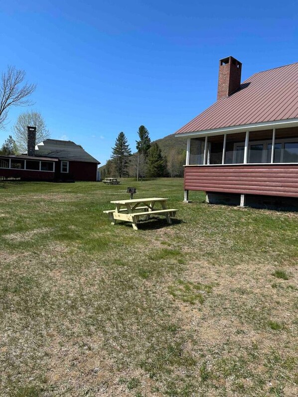 A picnic area with benches, a red building with a chimney, and a grassy field.