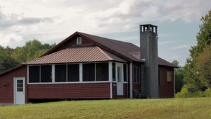Un bâtiment en bois rouge, doté d’une grande façade vitrée et d’une cheminée.