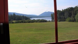 Une vue à travers une fenêtre sur un champ verdoyant, avec un lac et des montagnes en arrière-plan.
