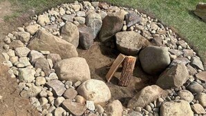 Un pozo de fuego de piedra circular con leña y un banco de madera.