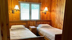 Una habitación con paneles de madera, dos camas, una mesita de noche y dos lámparas de pared.
