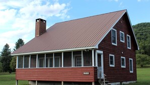 Een houten chalet met een metalen dak, een veranda en een schoorsteen.