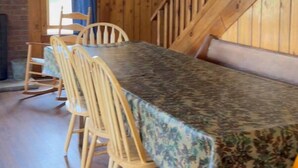 Een houten interieur met een eettafel gedekt voor vier personen, een trap en een raam met gordijnen.
