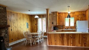 A spacious living area with a wooden floor, a dining table with chairs, a kitchen with wooden cabinets, and a refrigerator.