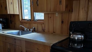 A kitchen with wooden cabinets, a stainless steel sink, a stove, and a window providing natural light.