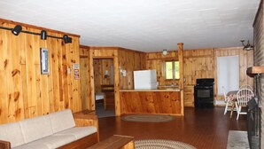 A wooden cabin interior with a living area, kitchen, and fireplace.
