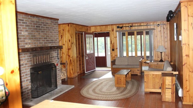 A cozy living room with a fireplace, wooden walls, a sofa, and a dining area.