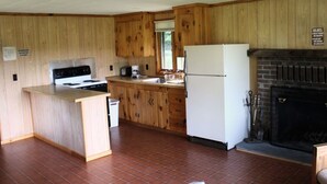 Eine Küche mit Holzausbau, einem weißen Kühlschrank, einem Herd und einem Kamin.