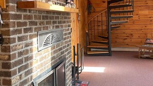 Ein rustikales Interieur mit Kamin aus Backstein, einer Wendeltreppe aus Holz und einer Erschließung mit Regalen.