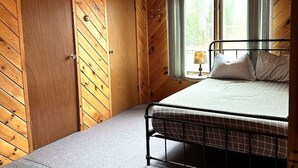 Ein Schlafzimmer mit Bett, einem Fenster mit Vorhängen, einem Oberlicht und Holzwänden.