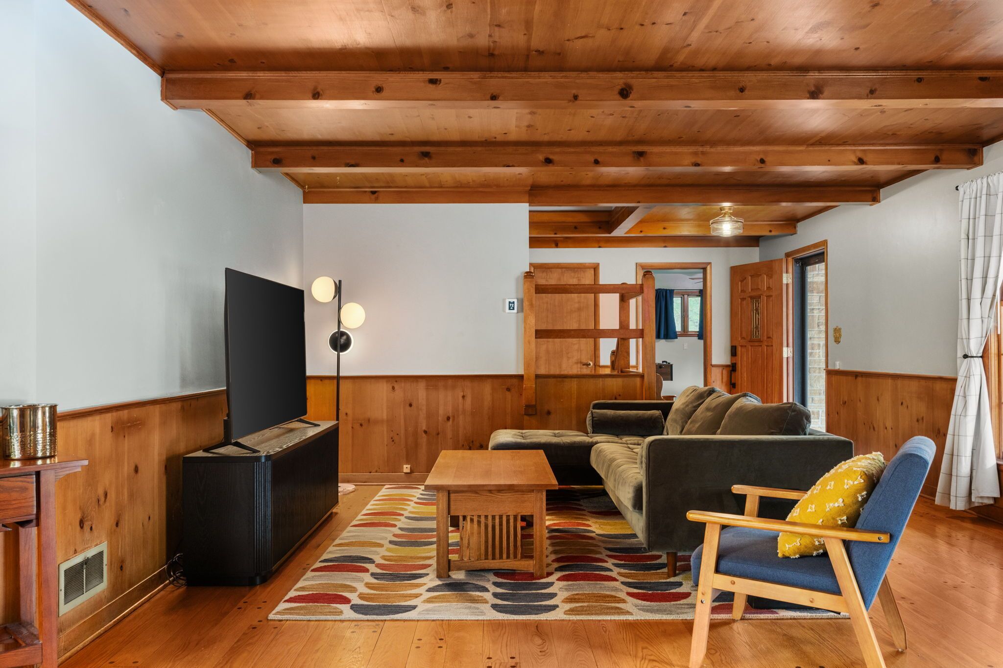 Una sala de estar acogedora con techo de madera, televisor, sofá, sillón y alfombra estampada.
