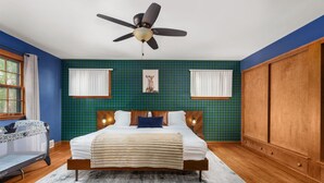 A bedroom with a bed, a ceiling fan, a window with curtains, a wooden wardrobe, and a plaid-patterned wall.
