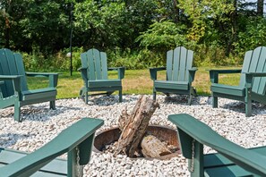 Un hogar de fuego rodeado de sillas Adirondack en un entorno natural.