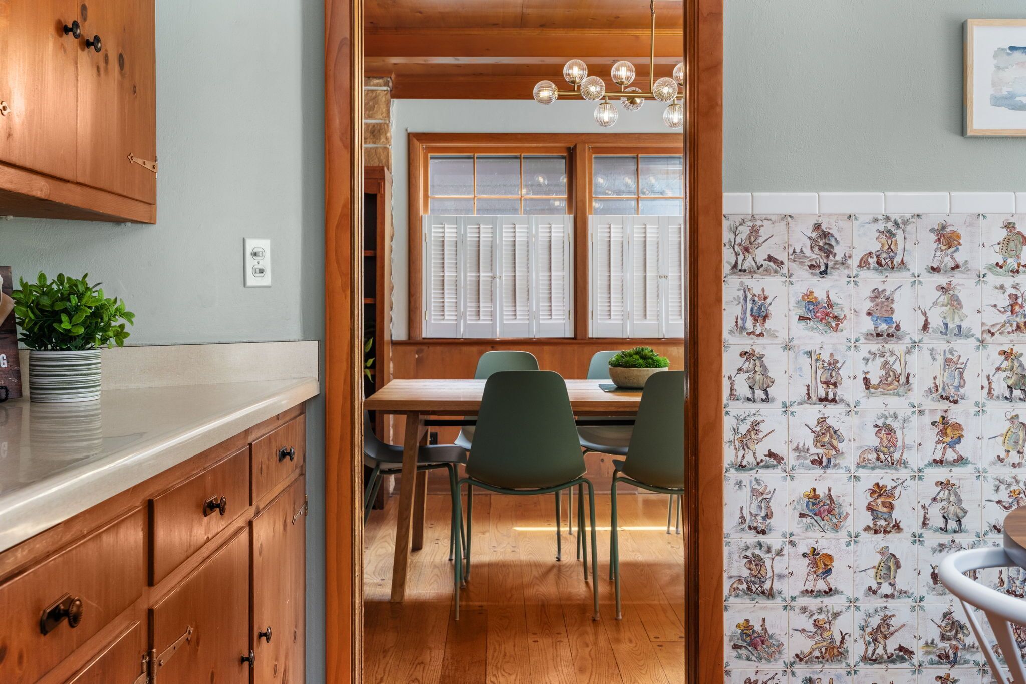 Una cocina con armarios de madera, una mesa de comedor con sillas y una ventana con contraventanas.