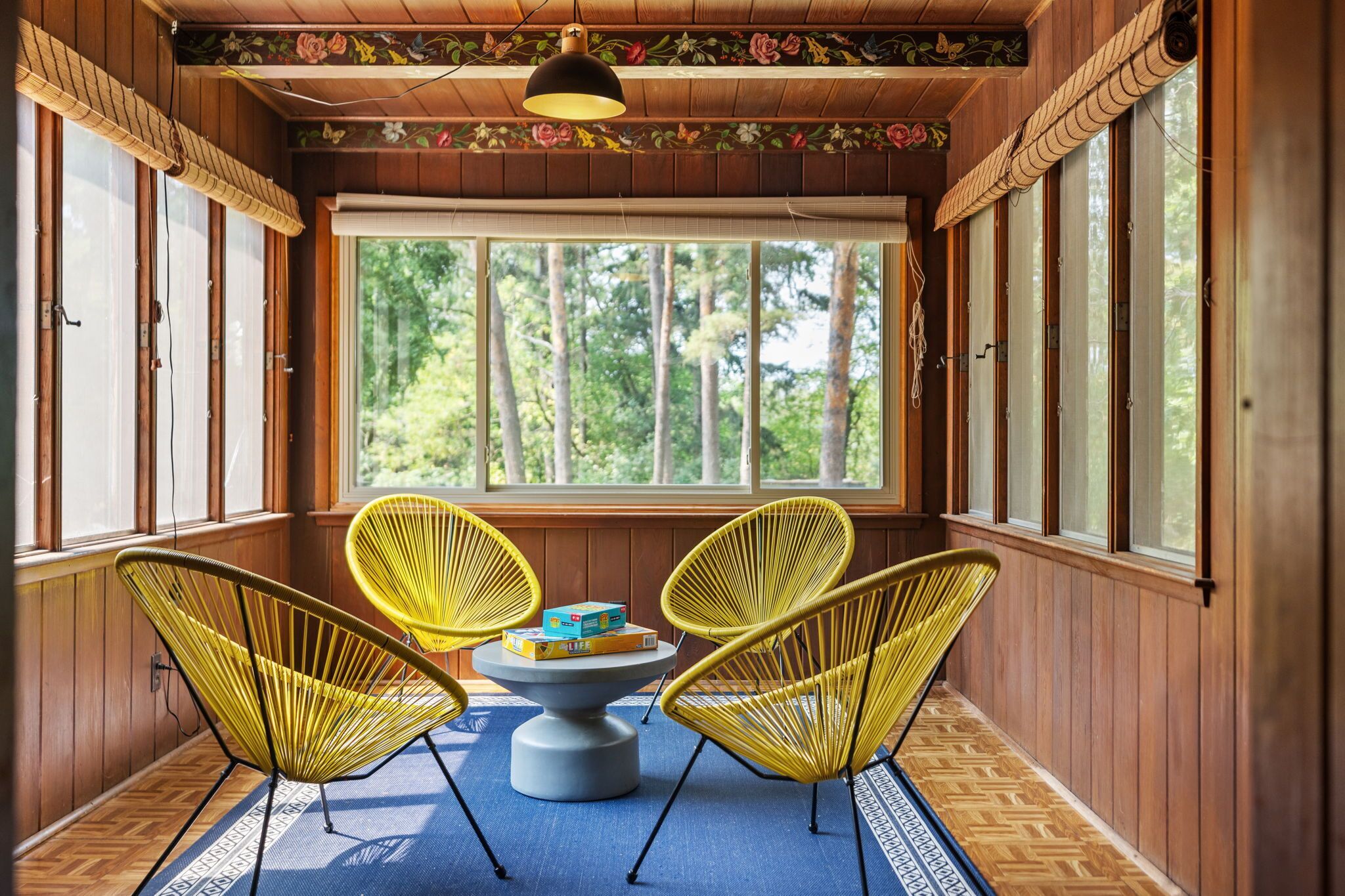 A room with wooden walls, large windows, and yellow chairs around a central table.