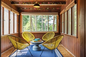 Una habitación con paredes de madera, ventanas amplias y sillas amarillas alrededor de una mesa central.