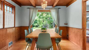 A dining room with a wooden table and chairs, a chandelier, and a view of trees through large windows.