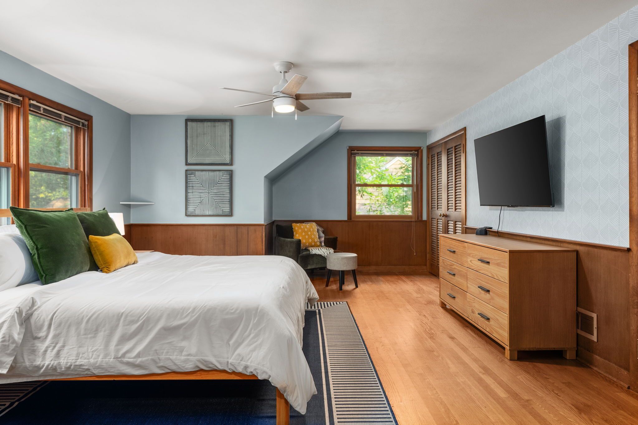 A bedroom with a bed, a desk, a chair, a television, and a ceiling fan.