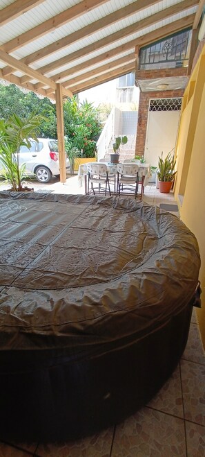 A covered outdoor area with a large black mat, a table with chairs, and a potted plant. - Bas de Villa en campagne (Le Lamentin)
