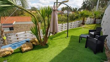 A backyard with artificial grass, a patio table and chairs, a white fence, and palm trees.